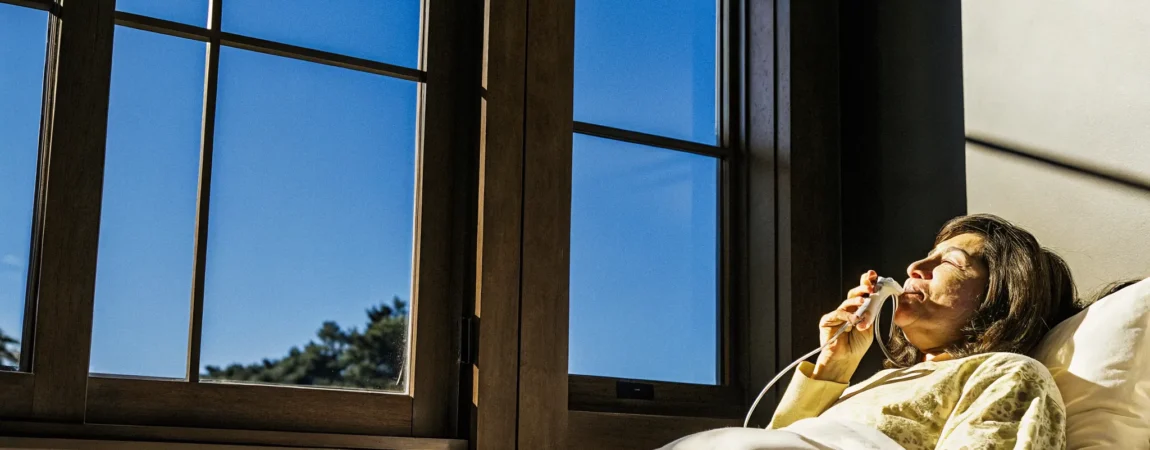 Sleep apnea patient holding a custom oral appliance, sitting up in bed with morning light